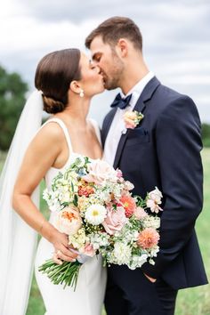 a bride and groom kissing each other in front of a green field with flowers on it