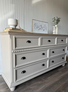 a white dresser sitting on top of a hard wood floor next to a vase filled with flowers