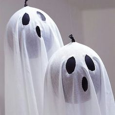 two white ghost costumes hanging from strings with black dots on their faces and arms, both in the shape of heads