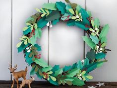 a christmas wreath with paper leaves and deer figurines next to it on a shelf