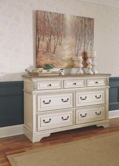 a white dresser sitting on top of a hard wood floor next to a painting above it