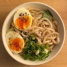 a bowl filled with noodles and eggs on top of a wooden table