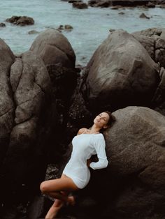 a woman is posing on some rocks by the water