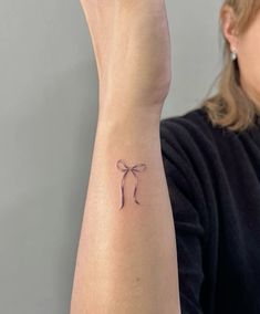 a woman's arm with a small bow tattoo on the left side of her wrist