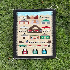 a quilted wall hanging on the grass in front of some buildings and cars,