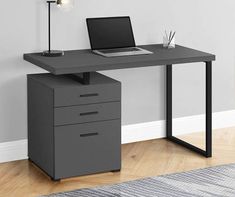 an office desk with a laptop on top and drawers underneath it, in front of a white wall