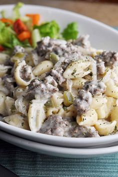 a white bowl filled with pasta and meat covered in sauce on top of a table