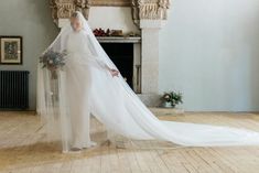 a woman in a white wedding gown and veil standing on a wooden floor next to a fireplace