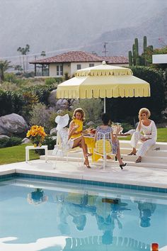 two women sitting under an umbrella next to a pool