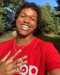 a young man with dreadlocks smiles and holds his hand up to his chest