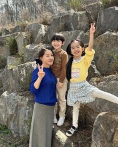 two girls and a boy are standing on some rocks with their hands in the air