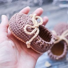 a hand holding a small crocheted baby bootie with a bow on it