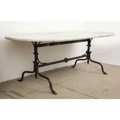 a marble top table with wrought iron legs and a white marble top, against a white wall