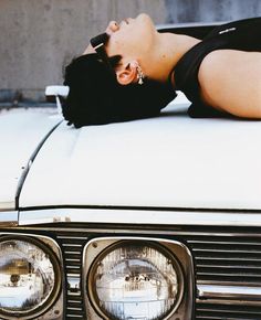 a woman laying on top of a white car with her head resting on the hood