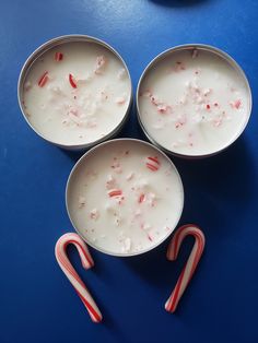 three bowls with candy canes in them on a blue table