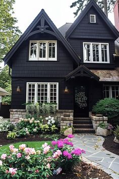 a black house with lots of windows and flowers in the front garden area on a sunny day