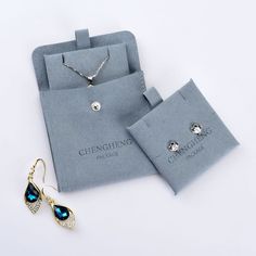 a pair of earrings and necklace sitting on top of a blue cloth bag next to it's packaging