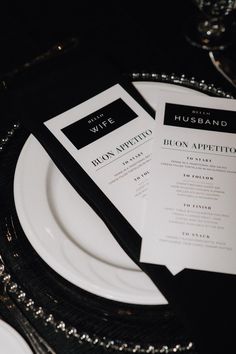 a table setting with black and white menus, silver place settings and wine glasses