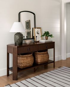 a wooden table with two baskets under a mirror and a lamp on top of it