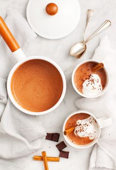 two cups of hot chocolate with marshmallows on the side and spoons