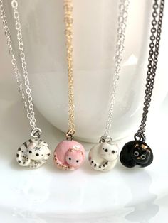 three necklaces with cats on them sitting in front of a white cup and saucer