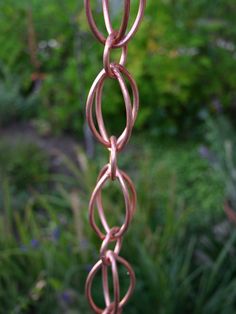 a close up of a metal chain hanging from a pole in a garden with flowers