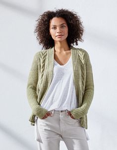 a woman standing in front of a white wall wearing a green sweater and cardigan