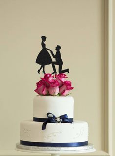 a wedding cake with pink roses and silhouettes on top, sitting on a table