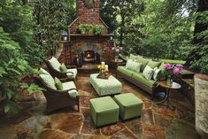 an outdoor living room with green furniture and a brick fire place in the center surrounded by greenery