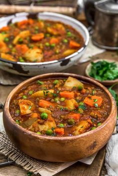 two bowls filled with stew and vegetables on top of a wooden table next to other dishes