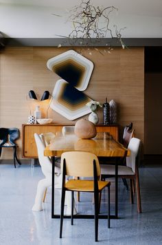 a dining room table and chairs in front of a wall with abstract artwork on it