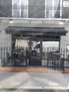 the front entrance to sticky mango restaurant with black wrought iron fence and tables on the sidewalk