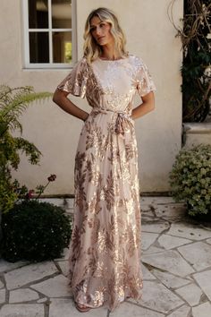 a woman standing in front of a building wearing a dress with gold leaves on it