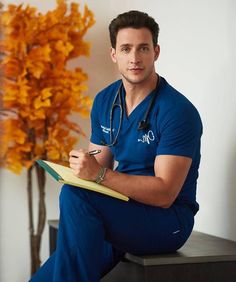 a male in a blue scrub suit is holding a pen and writing on a notepad