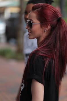 a woman with long red hair and sunglasses on walking down the street while wearing a black shirt