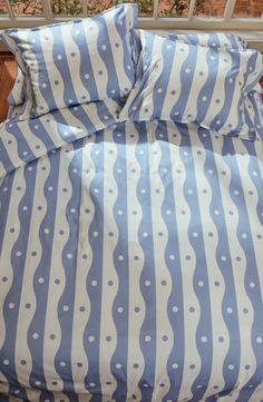 a bed with blue and white striped comforter on it's side, next to a window