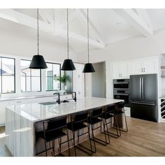 a kitchen with white cabinets and black pendant lights hanging from the ceiling over the island