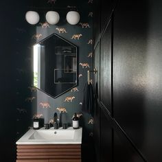 a bathroom with a mirror, sink and wallpapered animals on the black walls