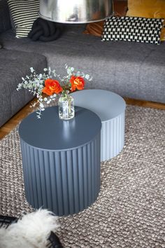 two vases with flowers sit on a table in front of a gray couch and rug