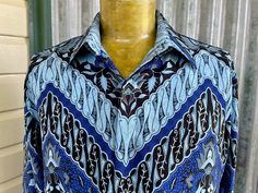 A seriously stunning 1990's vintage shirt for anyone who loves a bold design. This long sleeve shirt has a turn-down collar, hidden buttons, a front welt pocket and short side splits. It has an incredible Batik print of zig-zagged stripes of floral patterns in black, bright blue and pale blue. The inside of the body is lined. Pair with relaxed linen trousers for laid-back yet stylish look. Size Extra Large Measurements: Chest: 114 cm / 45 inches Shoulder: 51 cm / 20 inches Length: 75 cm / 29.5 inches Sleeve: 61 cm / 24 inches Polyester. This item is one of a kind. BUYING VINTAGE: While all care is taken to state any obvious faults, please note that when you buy a vintage or preloved item, they may show small signs of ageing, wear and/or repair. Visit my website   https://phoenixmenswear.co Blue Graphic Print Shirt With Spread Collar, Blue Spread Collar Shirt With Graphic Print, Blue Shirt With Graphic Print And Spread Collar, Blue Long Sleeve Top With Batik Print, Blue Retro Long Sleeve Shirt, Retro Blue Long Sleeve Shirt, Retro Long Sleeve Blue Shirt, Patterned Long Sleeve Shirt With Batik Print, Patterned Batik Print Long Sleeve Shirt