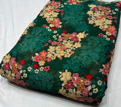 a green and red flowered blanket laying on top of a white sheet