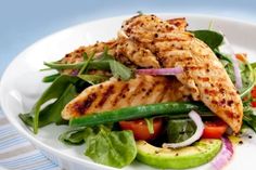 a white plate topped with chicken and veggies on top of a bed of lettuce