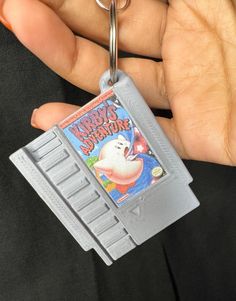 a person holding a nintendo gameboy keychain in their left hand, with the video game super mario on it