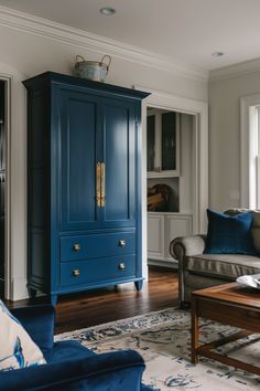 a blue armoire in a living room next to a couch and coffee table with pillows on it