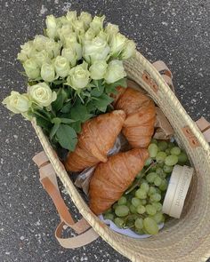 two croissants, grapes and flowers in a basket on the ground next to a bottle of wine