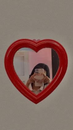 a woman taking a selfie in front of a heart shaped mirror with her phone