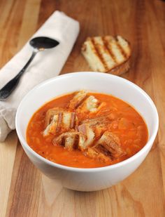 there is a bowl of soup on the table next to some grilled cheeses