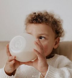 a little boy holding a bottle in his hand and looking at the camera while sitting on a couch