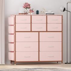 a pink dresser with lots of drawers next to a lamp and flowers on the table