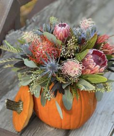 a pumpkin filled with flowers sitting on top of a wooden bench